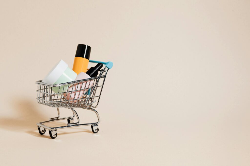 A minimalist image of a mini shopping cart filled with cosmetics on a beige background, ideal for e-commerce concepts.